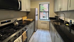 Une cuisine compacte équipée d’une cuisinière, d’un four à micro-ondes, d’un réfrigérateur et d’une fenêtre donnant sur un immeuble en briques.