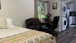 Une chambre d’hôtel équipée d’un lit, d’un bureau, d’une chaise, d’une machine à laver et d’une fenêtre avec des rideaux.