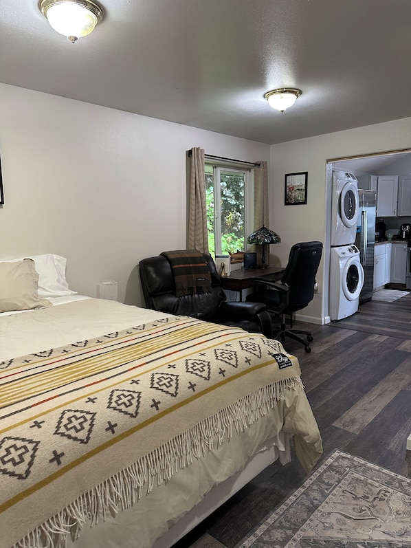 A hotel room with a bed, a desk, a chair, a washing machine, and a window with curtains. - Cozy studio apartment with waterfront view (Cordova)