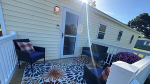 A covered porch with two chairs and a table, a decorative rug, and a small garden with purple flowers. - Charming family friendly 3-bedroom house in  Painter with AC and outdoor patio (Painter)