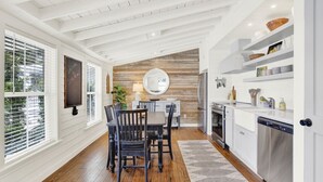 Eine moderne Küche mit weißen Schränken, einer Wand in Holzoptik und einem Essbereich mit rundem Tisch und Stühlen.