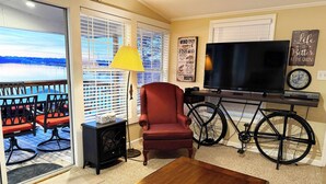 A living room with a TV, a red chair, a bicycle, and a view of the outdoors. - Waterfront! Prime Location, Clean, Swimming Pool, Fishing Dock, WIFI (George town)