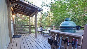 Une terrasse en bois dotée d’un espace salon couvert, d’un grand barbecue et d’ustensiles de barbecue.