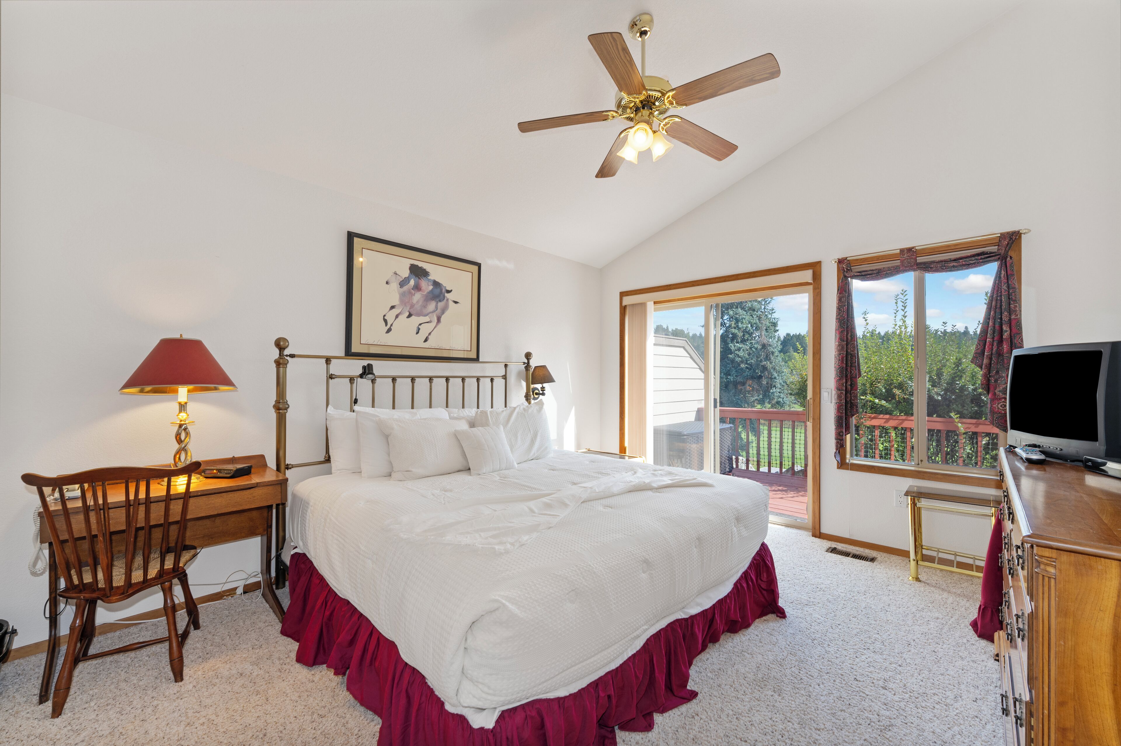 A bedroom with a bed, desk, chair, TV, and a ceiling fan.