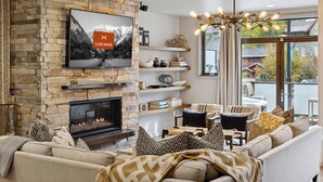 A modern living room with a stone fireplace, a large flat-screen TV, and a cozy seating area with a sofa and chairs.