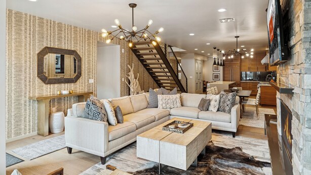 A modern living room with a sectional sofa, a coffee table, a fireplace, and a staircase leading to an upper level.