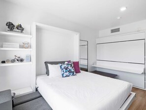Une chambre à coucher moderne, équipée d’un lit, d’étagères intégrées, d’une armoire et d’une petite table.