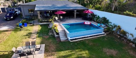 A residential property with a swimming pool, outdoor seating, and a covered patio.