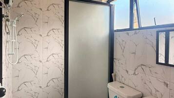 A bathroom with a shower, toilet, and sink, all with marble-like wall tiles.
