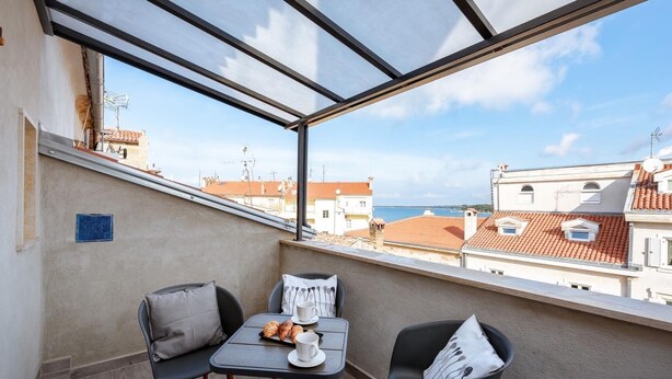 Ein Balkon mit Tisch, zwei Stühlen und Blick auf das Meer und die Bebauung.
