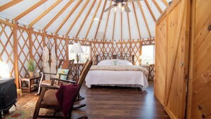 A yurt interior with a bed, rocking chair, and a small table with a lamp. - Monarch Yurt: Luxury Glamping Near Hocking Hills Trails with King Bed and Breakfast (Logan)