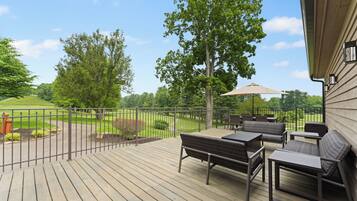 A wooden deck with outdoor furniture, a view of a golf course, and a tree.