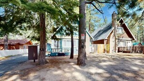 A rustic cabin with a wooden exterior, surrounded by trees and a gravel driveway. - Sunny Retreat | Near Beaches & Trails | Sleeps 6 (South Lake Tahoe)