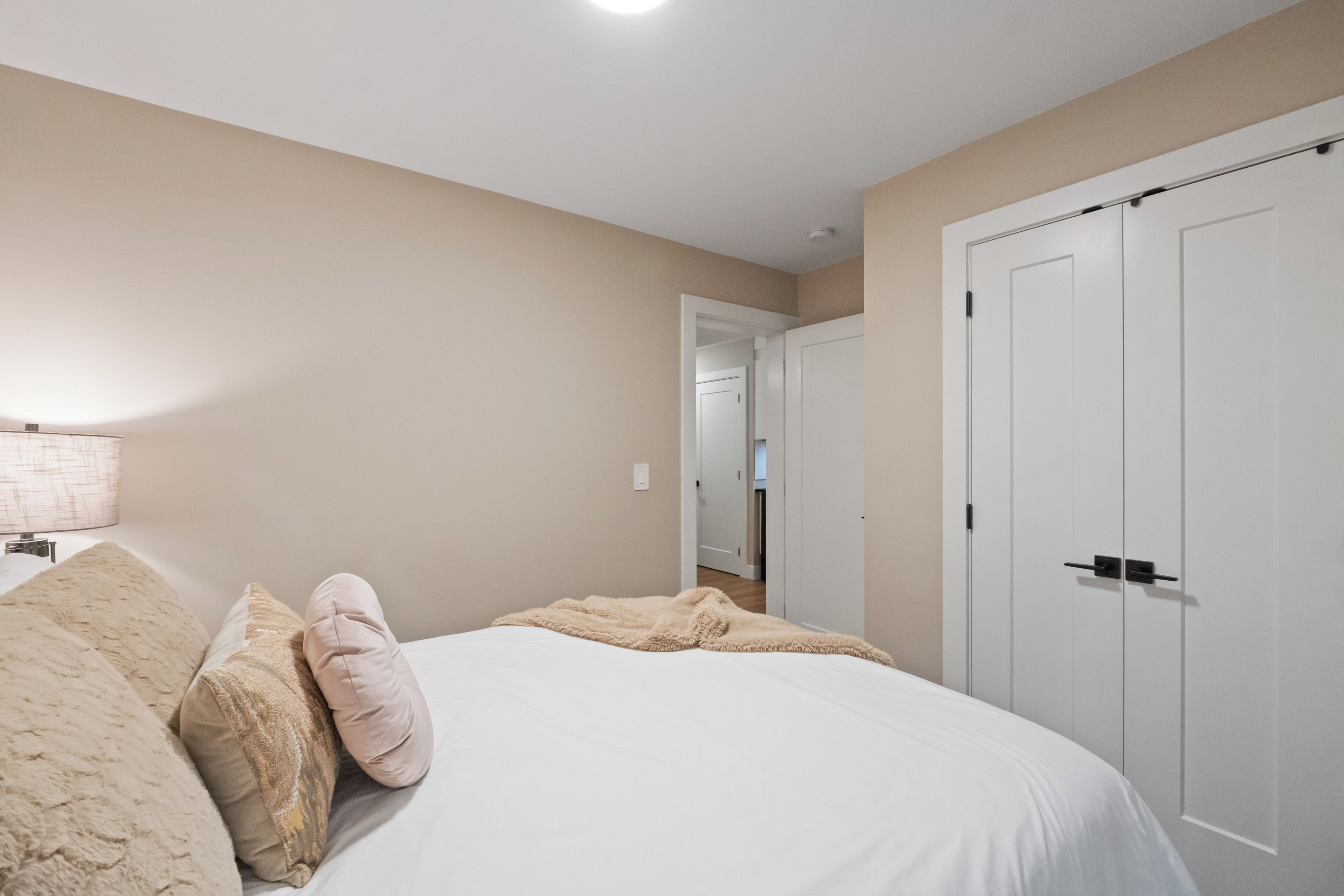 A bedroom with a large bed, a white door, and a hallway leading to another room.