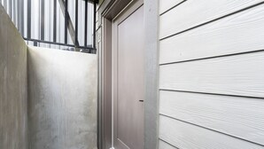 Un estrecho pasillo exterior con una escalera de metal y una puerta cerrada.