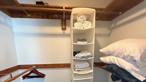 Un petit placard bien rangé, avec des étagères pour les vêtements pliés, une tringle pour suspendre les vêtements et un bac de rangement.