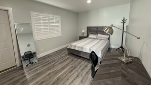 Une chambre à coucher avec un lit, une table de chevet, une lampe, un porte-manteau et un miroir.