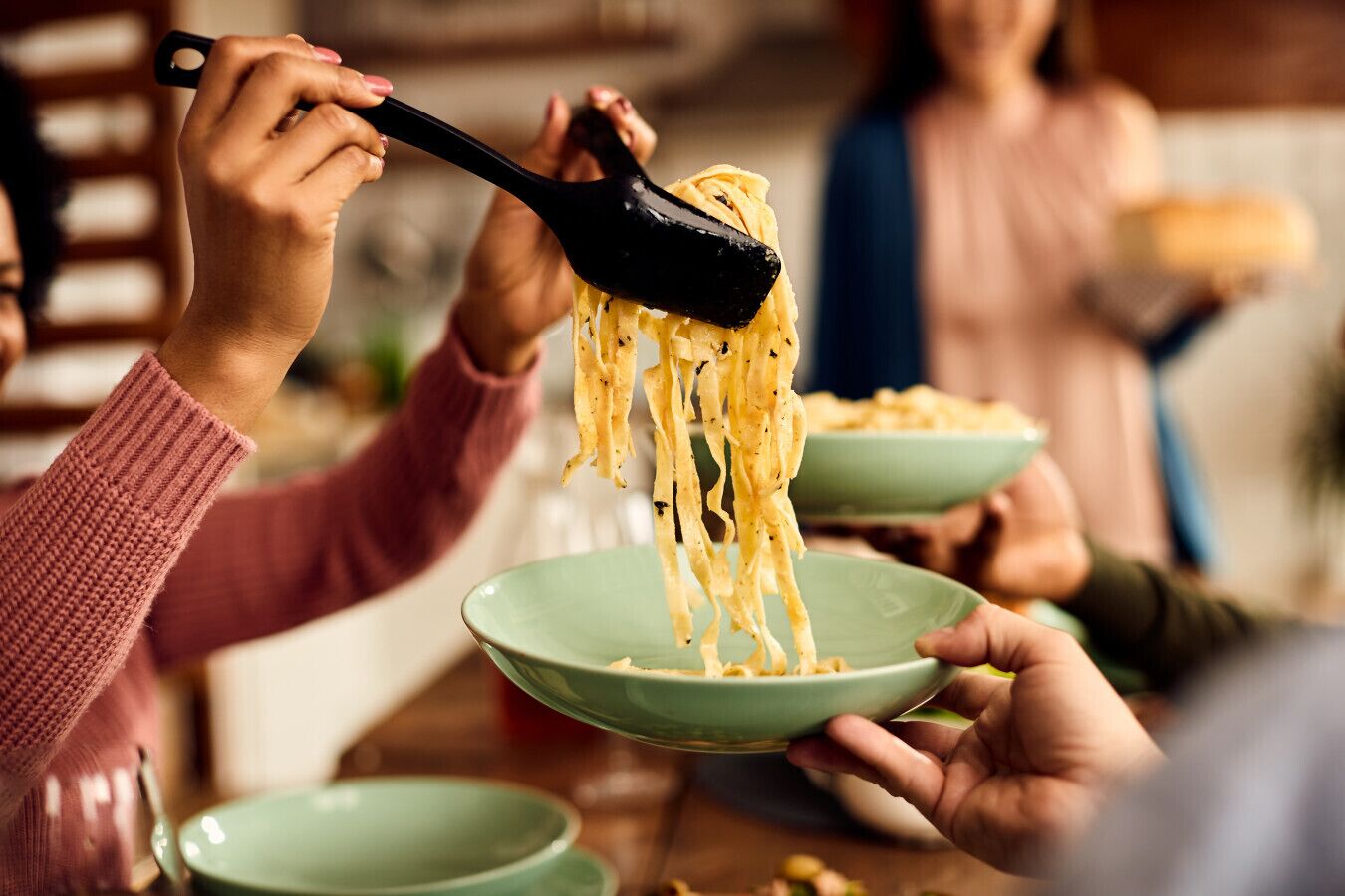 Une table à manger avec plusieurs assiettes vertes et une spatule noire servant à soulever des spaghettis.