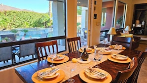 A dining table set for four with a view of a pool and greenery outside. - Coachella Walkable | Tuscan Villa | Pool Sleeps 12 (Indio)