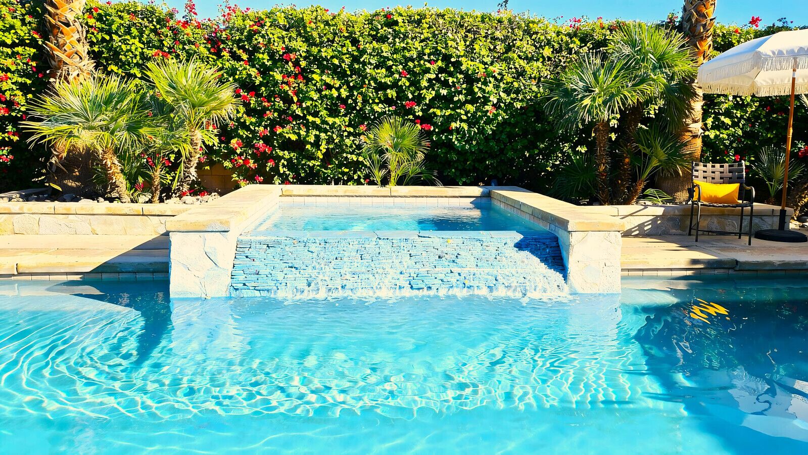 Une piscine avec un bord en pierre et une haie en arrière-plan.