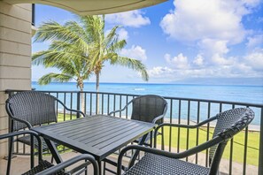 A balcony with a table and chairs, overlooking a beach with palm trees and the ocean.