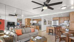 A spacious living room with a sofa, coffee table, and dining area with chairs and a table. - Kahana Reef 210 (Lahaina)
