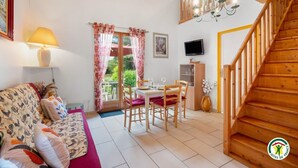 Un salon chaleureux avec un canapé, une table à manger et des chaises, un escalier et un téléviseur fixé au mur.