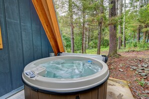 Uma banheira de hidromassagem em área arborizada, com deck de madeira e parede azul.