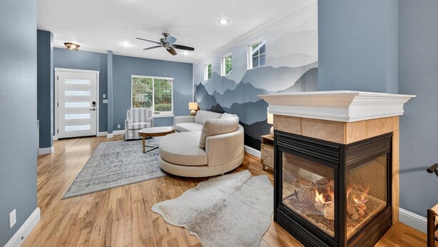 A modern living room with a fireplace, a ceiling fan, and a large window.