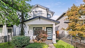 A two-story house with a front porch, a small garden, and a metal fence.