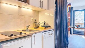 Ett modernt kök med diskmaskin, vattenkokare och kaffebryggare. Det finns ett fönster med utsikt över omgivningen.