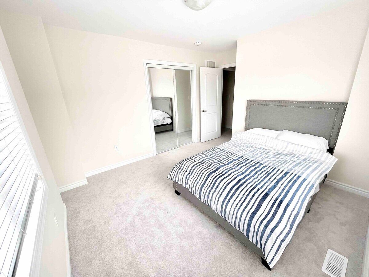 A bedroom with a bed, carpeted floor, and a door leading to another room.