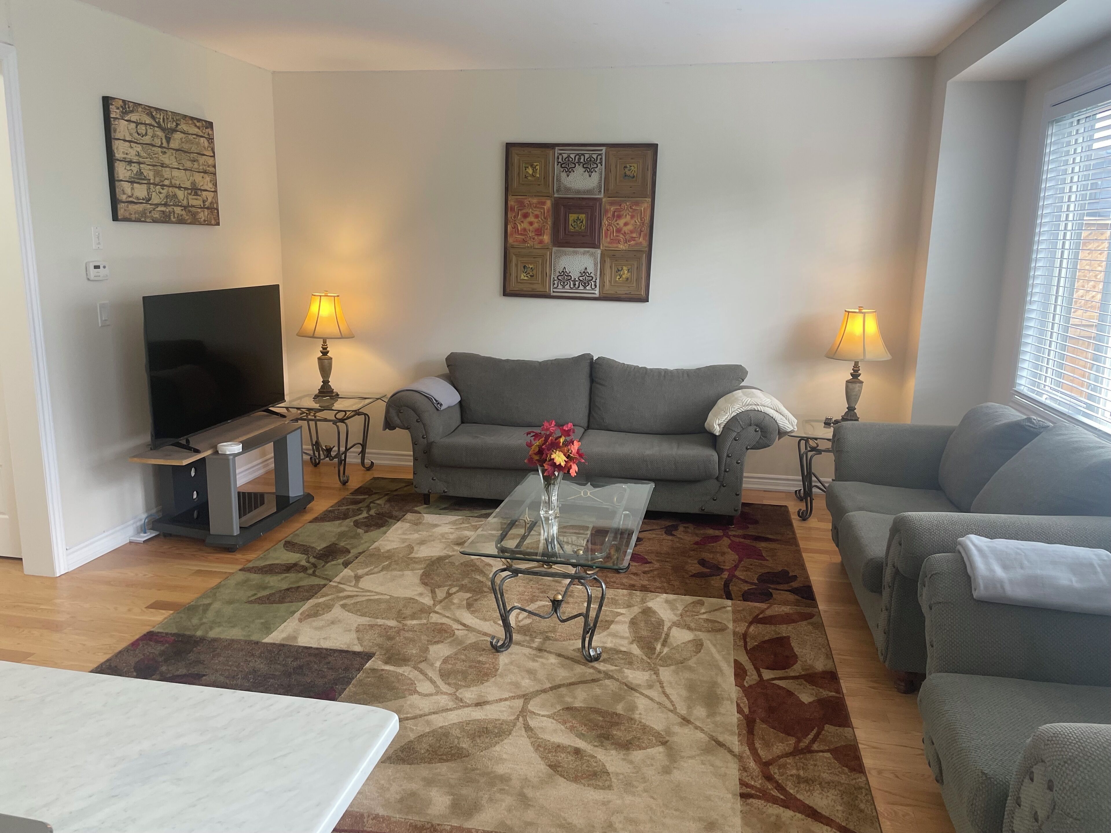 A living room with a sofa, two armchairs, a coffee table, a TV, and two lamps.