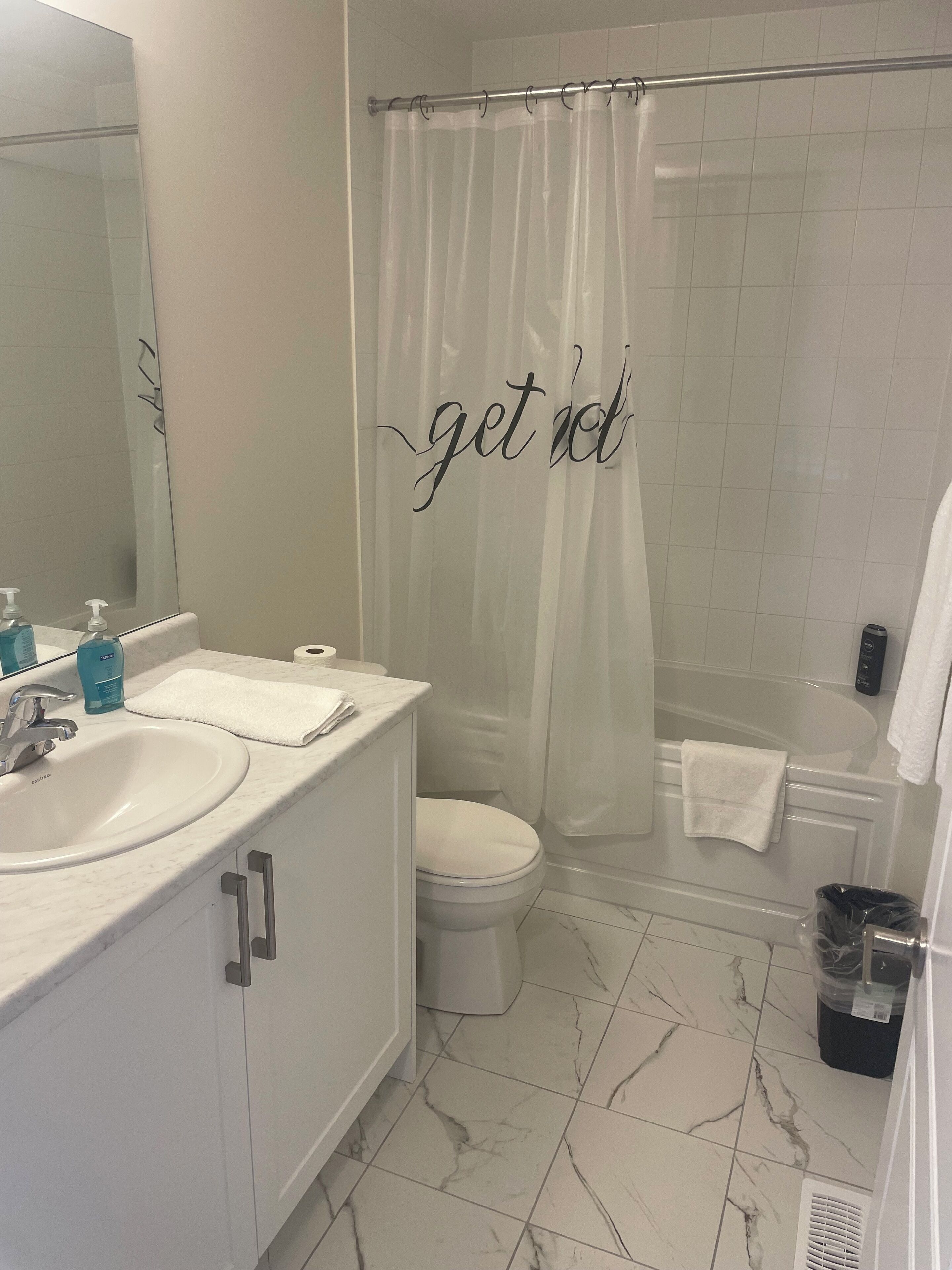 A modern bathroom with a white sink, mirror, and toilet. A shower curtain with the text "get dol" hangs in the shower area.