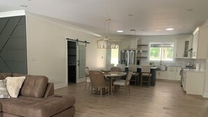 Een moderne open woon- en eetruimte met een bruine leren bank, een eettafel met stoelen en een keuken met witte kasten en roestvrijstalen apparatuur.