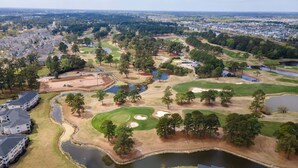 Un parcours de golf comportant de nombreux bunkers, des obstacles d’eau et une zone résidentielle avec des immeubles à plusieurs étages.