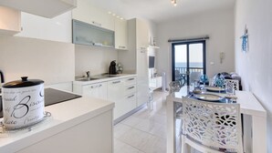 Una cucina moderna con mobili bianchi, un'area pranzo vista mare e un balcone con posti a sedere esterni.