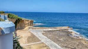 Vista costiera con un litorale roccioso, una struttura in cemento e un cielo azzurro limpido.