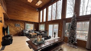 A spacious living room with a wooden ceiling, large windows, a fireplace, and a Christmas tree. - Spacious Cabin in LOTN- Great for ORV, Snowmobile, Golf, Ski or family getaways! (Mancelona)