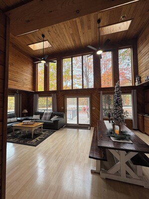 Un salon spacieux avec un plafond en bois, de grandes fenêtres, une cheminée et un coin salon confortable.
