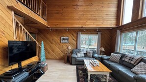 A cozy living room with a wooden interior, a television, a sofa, a coffee table, and a small Christmas tree. - Spacious Cabin in LOTN- Great for ORV, Snowmobile, Golf, Ski or family getaways! (Mancelona)