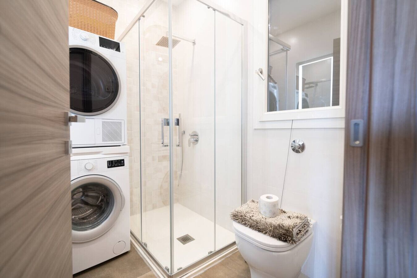 Ein kleines Badezimmer mit Waschmaschine, einer Duschkabine und einem WC mit einem flauschigen Teppich.