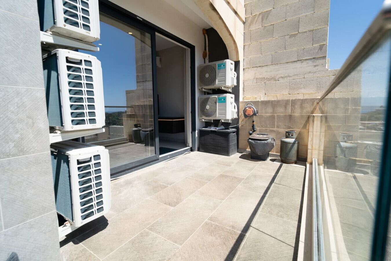 A balcony with air conditioning units, a trash bin, and a water dispenser.