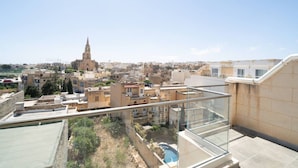 A cityscape with a prominent church tower, residential buildings, and a rooftop pool area. - Ghajnsielem Retreat 4 Bedrooms Panoramic Terrace (Ghajnsielem)