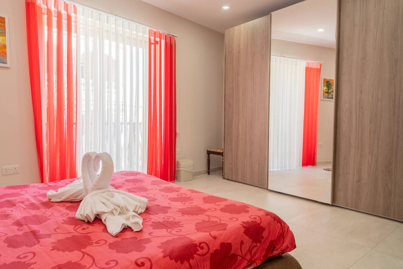 A hotel room with a bed, a mirror, and a red curtain.