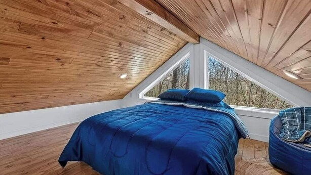 Un dormitorio con techo inclinado, un ventanal grande y una cama con ropa de cama azul.