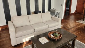 Uma sala de estar com um sofá bege, uma mesa de centro de madeira com uma planta e uma parede listrada em preto e branco.