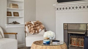 Een woonkamer met een open haard, een ronde salontafel met een pot en boek, een witte fauteuil en een boekenkast met boeken en een schedel decoratie.