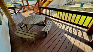 Eine Holzterrasse mit Picknicktisch und Bänken, mit Blick auf eine Rasenfläche und Gebäude.