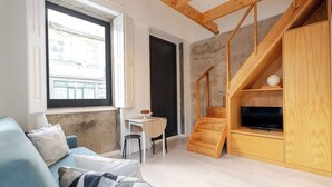 A modern living room with a blue sofa, a wooden TV stand, and a staircase.